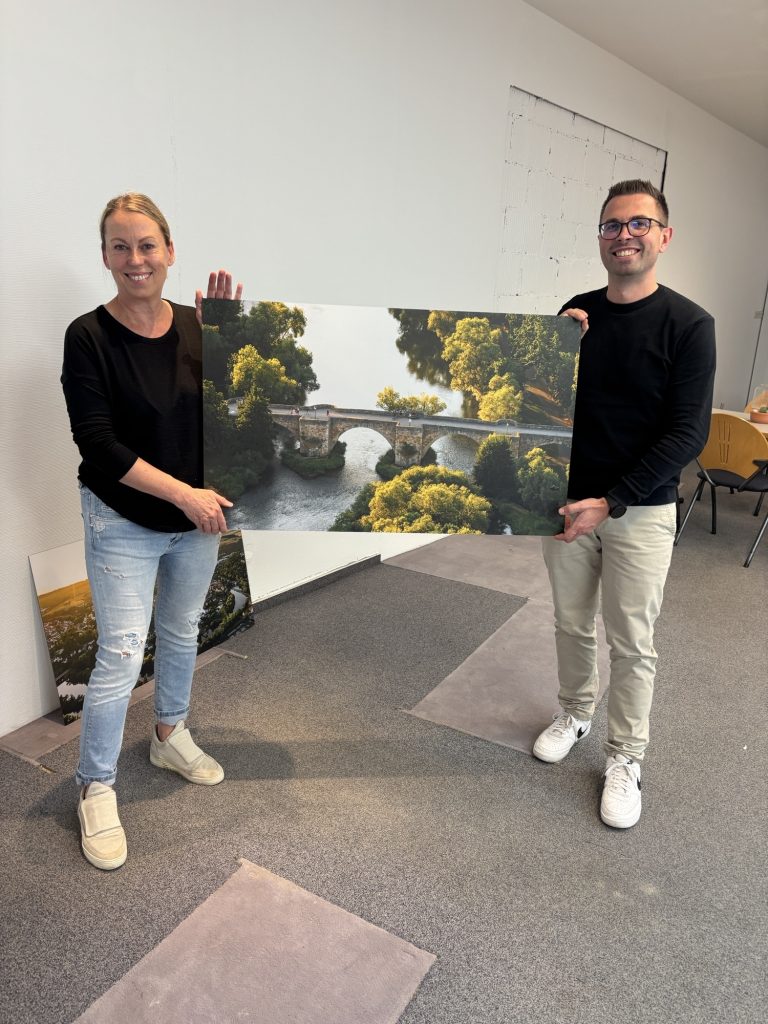 Das Foto zeigt Simone Wille (Agentur bb10) und Alexander Dupont (Citymanager der Stadt Melsungen) bei den Vorbereitungen am 1. Oktober, wie sie gemeinsam ein Motiv der Ausstellung in den neuen Räumen präsentieren. (Bildrechte: Stadt Melsungen)