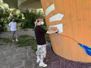 Mit ruhiger Hand und viel Kreativität setzt ein Schüler der Gesamtschule Melsungen die ersten Farbakzente auf der Betonstütze unter der Schlossbrücke. Gemeinsam entsteht ein Kunstwerk, das einen bislang als Angstraum wahrgenommenen Bereich aufwerten soll. Foto: Stadt Melsungen / Alexander Dupont