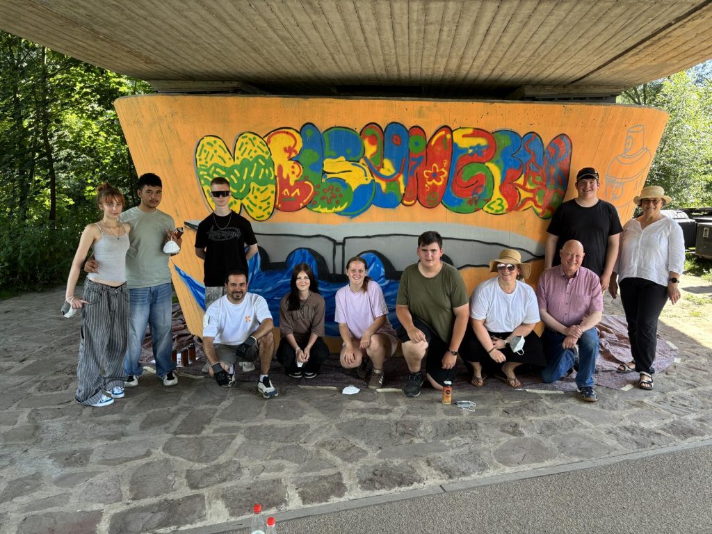 Schülerinnen und Schüler der Gesamtschule Melsungen gestalten gemeinsam mit den KOMPASS-Ansprechpartnern Elke und Wolfgang Schrammel sowie Graffiti-Künstler Marcel de Medeiros eine Betonstütze der Schlossbrücke. Die Aktion ist Teil des KOMPASS-Prozesses und soll dazu beitragen, einen als Angstraum wahrgenommenen Bereich am Fuldaufer freundlicher und einladender zu gestalten. Foto: Stadt Melsungen / Alexander Dupont