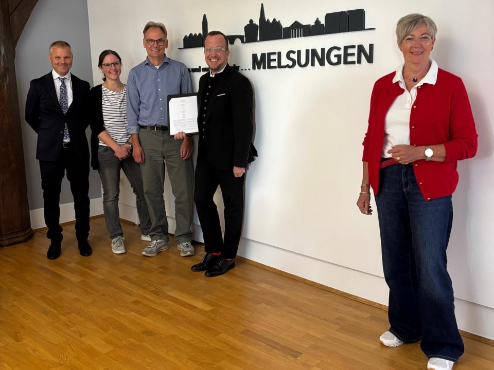 Gemeinsam für mehr Solarenergie in Melsungen: Darius Maloschek, Sarah Link, Thomas Flügge, Bürgermeister Timo Riedemann und Erste Stadträtin Ulrike Hund präsentieren vor der Melsungen-Silhouette die Kooperationsvereinbarung zwischen der Stadt Melsungen und der cdw Stiftung. Mit der geplanten 360-kWp-Photovoltaikanlage am Waldschwimmbad und einer Anschubfinanzierung von rund 500.000 Euro wird der Grundstein für weitere Klimaschutzprojekte in Melsungen gelegt.